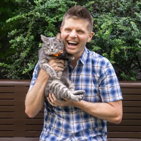 Ein lachender Mann hält eine grau-weiß gestreifte Katze