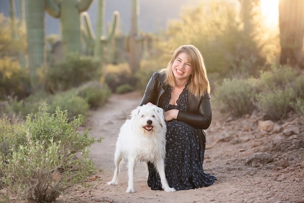 Woman and dog smile on desert path with cactuses in background