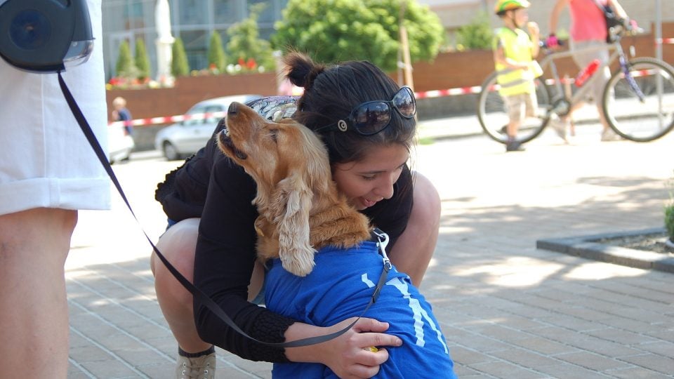 A woman crouches and hugs a therapy dog outside a facility.