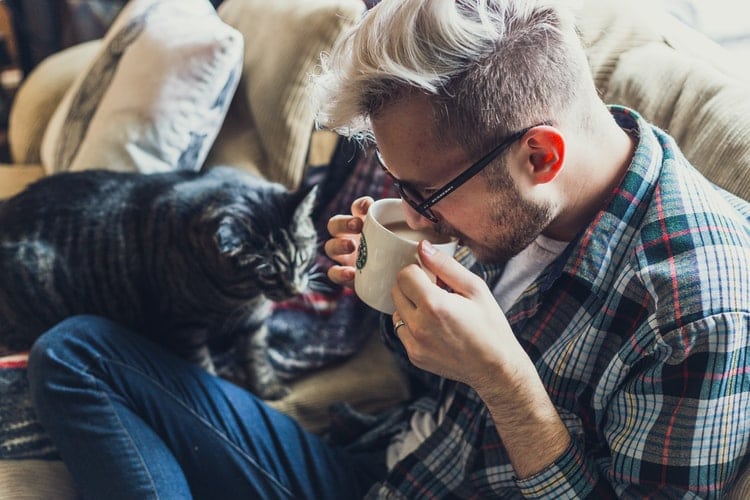A man drinks coffee with his cozy cat
