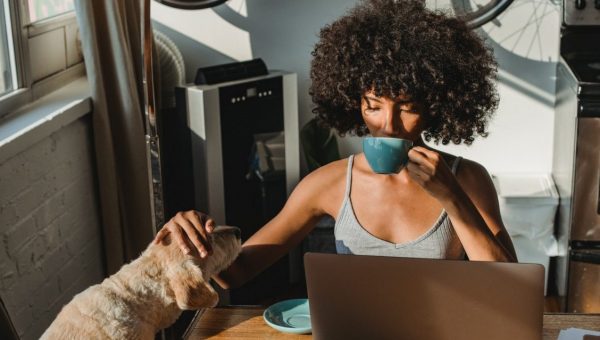dog mom drinking from mug with pup and laptop