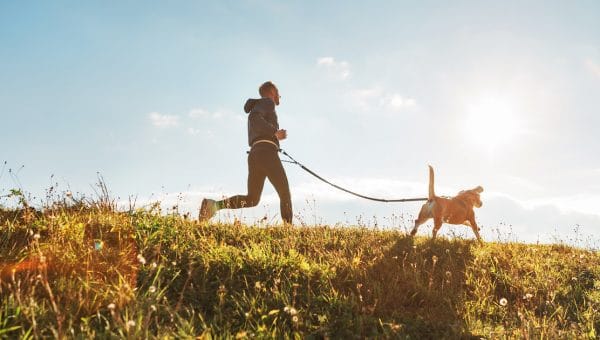 person running outside with dog on leash attached to belt
