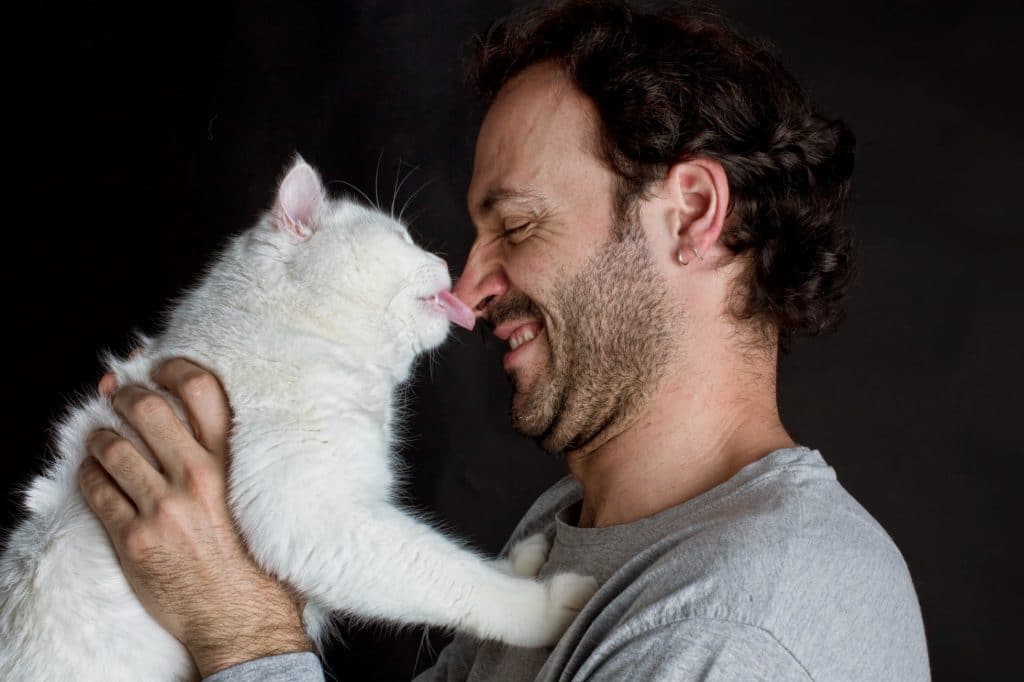 man getting licked on the nose by a  white cat he's holding
