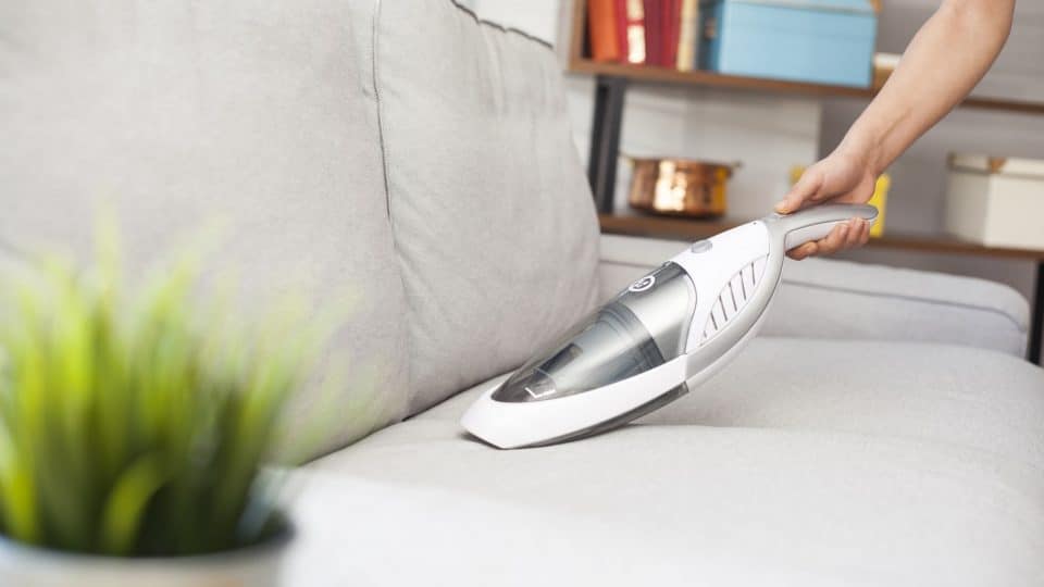 person using handheld vacuum on a couch