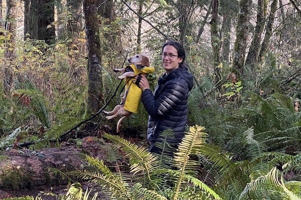 Person lifts dog in raincoat over large puddle in forest