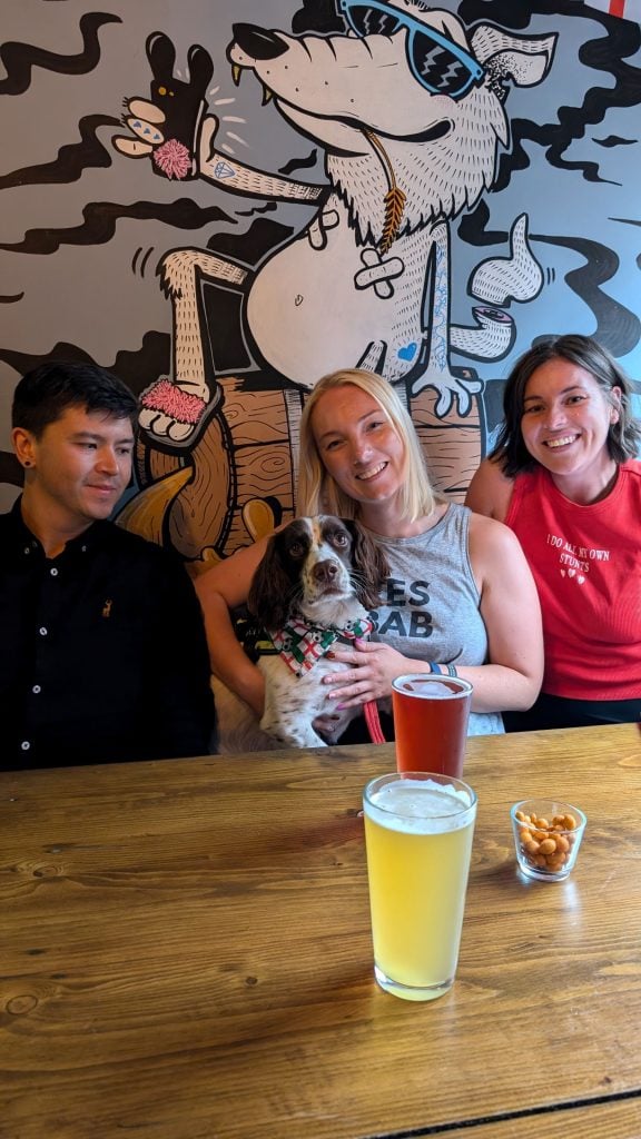 A group of friends iwth a dog in front of a wolf mural at The Wolf pub, Birmingham
