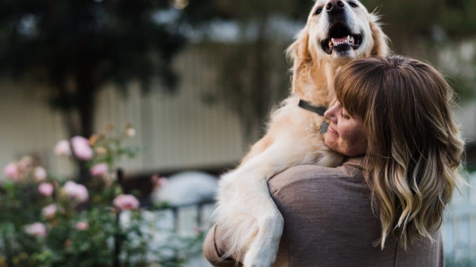 woman smiles and hugs golden retriever
