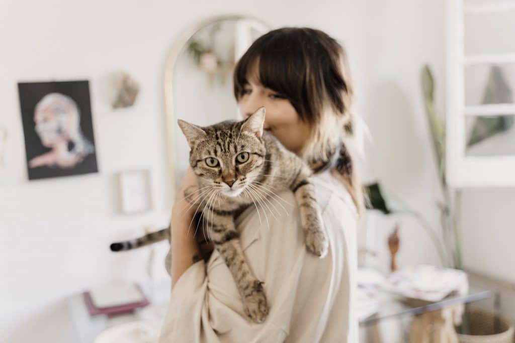 a woman holds her cat on her shoulder