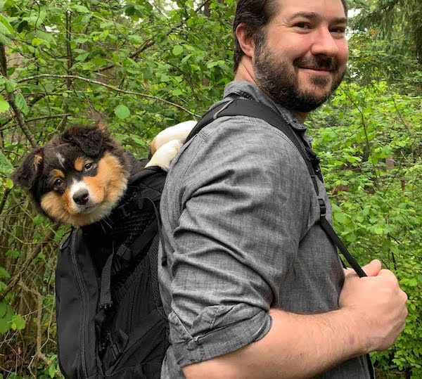 Man in forest with puppy in backpack