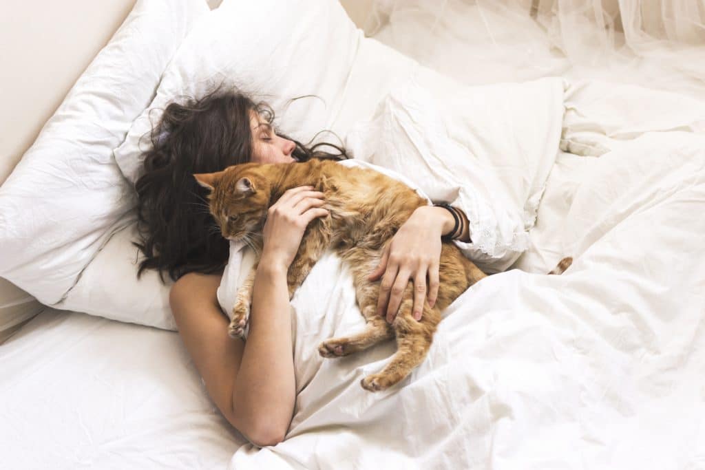 Woman asleep in bed joined by her cat