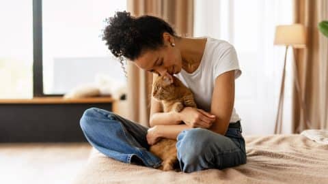Woman snuggling cat on bed