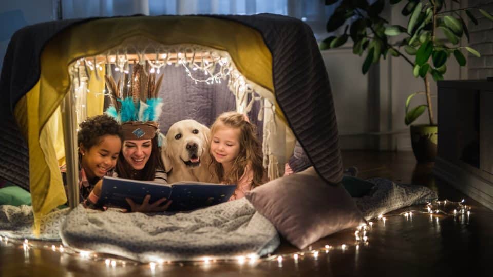 Family reading in tent with fairy lights and dog