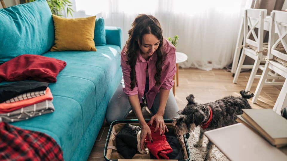 Person packing clothes into suitcase while dog watches
