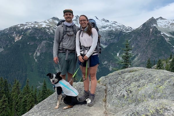 Two people standing on a rock with dog wearing Swamp Cooler vest