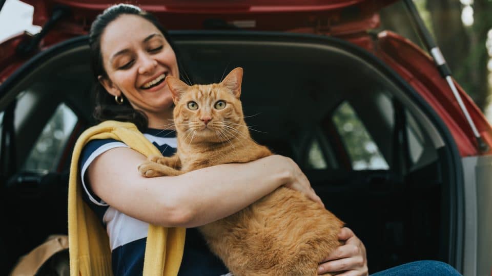 Woman sitting on back of car holding cat