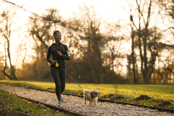 Woman jogging with dog in park at sunset