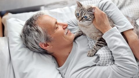 older man hugging a grey and white cat