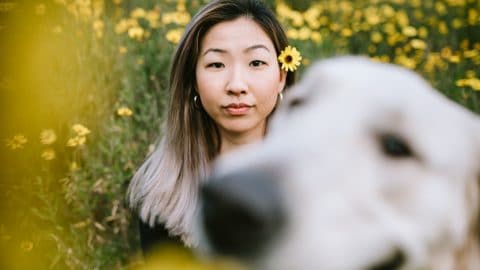 A happy Korean woman enjoys spending time with her Golden Retriever outdoors in a Los Angeles county park in California on a sunny day. She looks at the camera for a portrait, her pup photobombing the picture