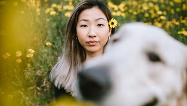 A happy Korean woman enjoys spending time with her Golden Retriever outdoors in a Los Angeles county park in California on a sunny day. She looks at the camera for a portrait, her pup photobombing the picture