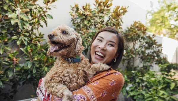 A shot of a young, Asian woman smiling at the camera with her dog.