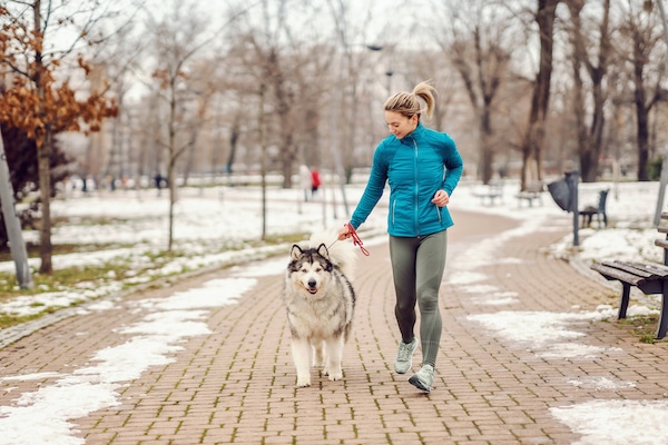 Sportswoman running with her dog in a park on cold winter day.