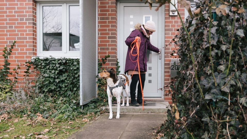 Woman leaving house with dog on long leash