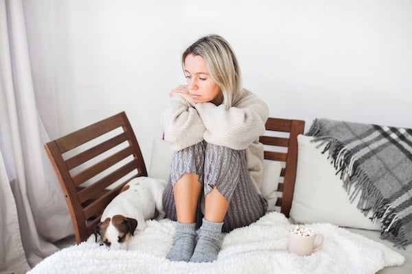 Sad-looking woman sitting on couch next to puppy