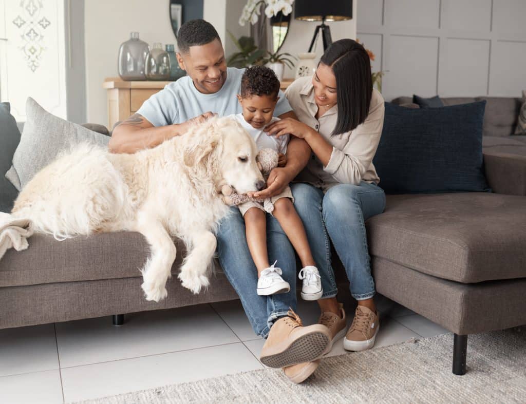 A happy mixed race family of three relaxing on the sofa with their dog. Loving black family being affectionate with a foster animal. Young couple bonding with their son and rescued puppy at home