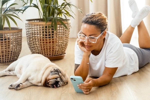 Woman laying on floor with dog while texting on phone