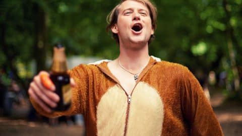 Shot of a young man drinking outside while dressed in a bear suit