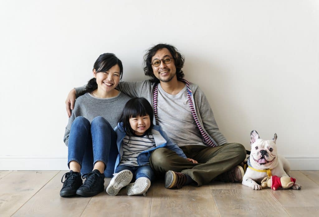 young Asian couple with son sit on the floor of their new home with their Bulldog