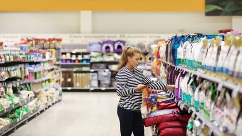 Woman shopping in supermarket reading pet food product information.