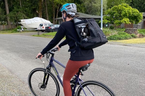 Woman rides bike with dog in backpack