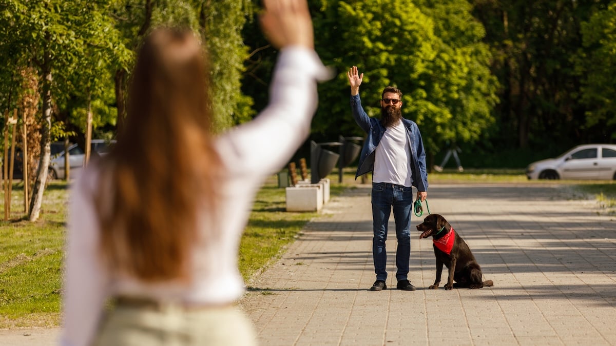 Person waving to man with dog across the street