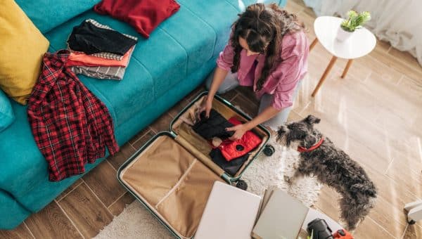 Woman packing suitcase while dog looks on