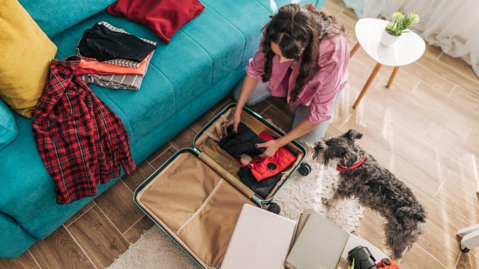 Woman packing suitcase while dog looks on