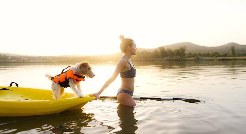 Photo of a young woman ready to kayaking on the lake with her dog
