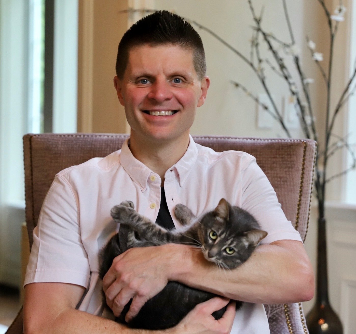 smiling man holding a grey and white striped cat