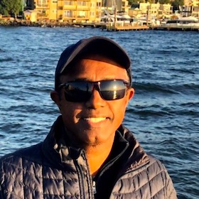 smiling man wearing sunglasses with a shore in the background