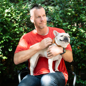 smiling man holding a small white dog on his lap
