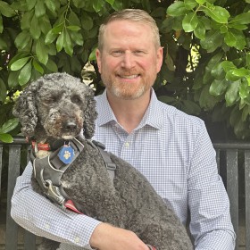 smiling man holding a curly haired grey dog